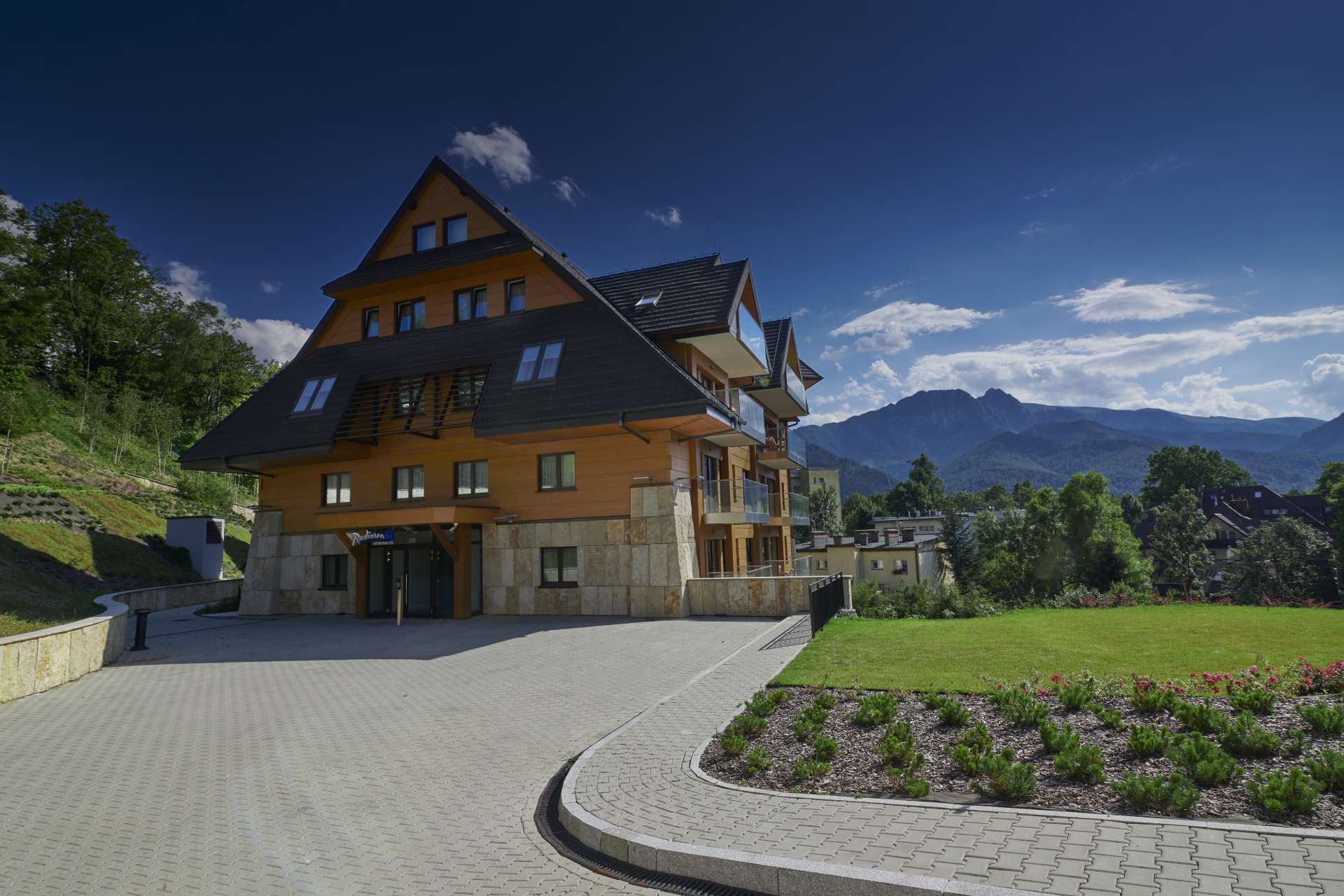 Radisson Residences Zakopane — elewacja budynku w stylu góralskim z drewnianą i kamienną okładziną oraz widokiem na Giewont