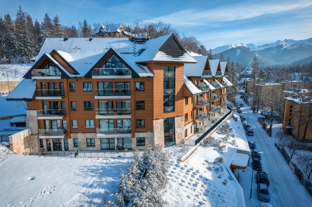 Radisson Residences Zakopane — budynek w zimowej scenerii ze śniegiem na dachu, balkonami ze szklanymi balustradami i widokiem na Tatry