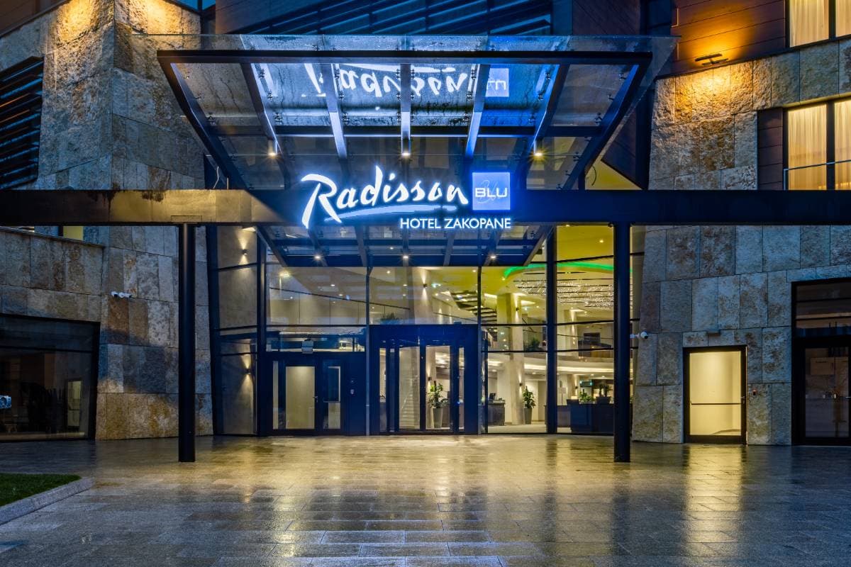 Radisson Residences Zakopane — główne wejście do hotelu Radisson Blu Zakopane nocą z podświetlonym logo i szklanym daszkiem
