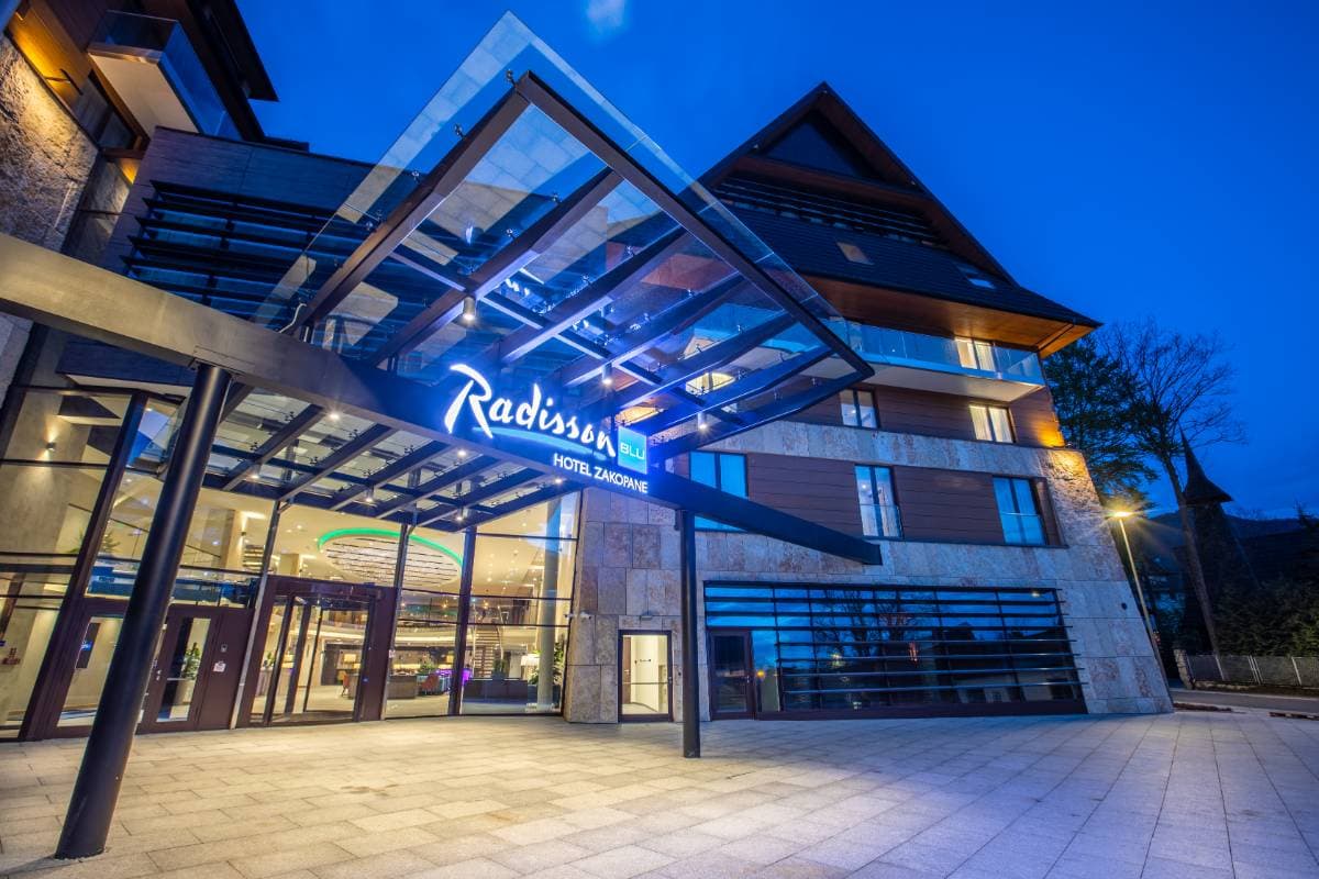 Radisson Residences Zakopane — wejście do hotelu Radisson Blu Zakopane o zmierzchu z podświetloną elewacją kamienno-drewnianą
