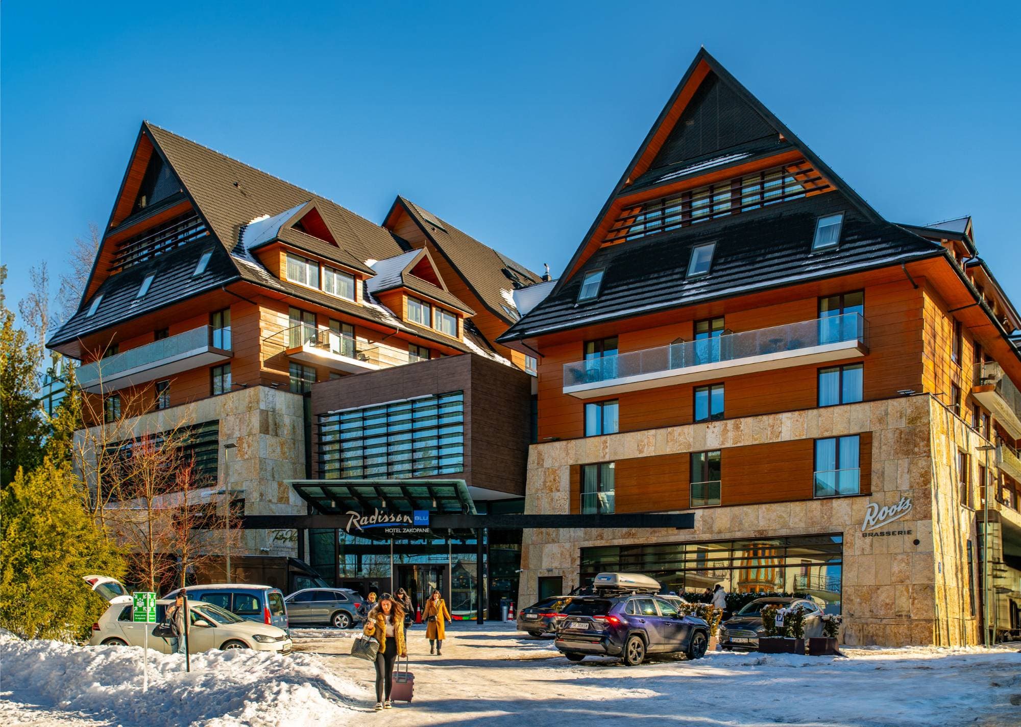 Radisson Residences Zakopane — elewacja budynku w słoneczny zimowy dzień z wejściem Radisson Blu i restauracją Roots Brasserie